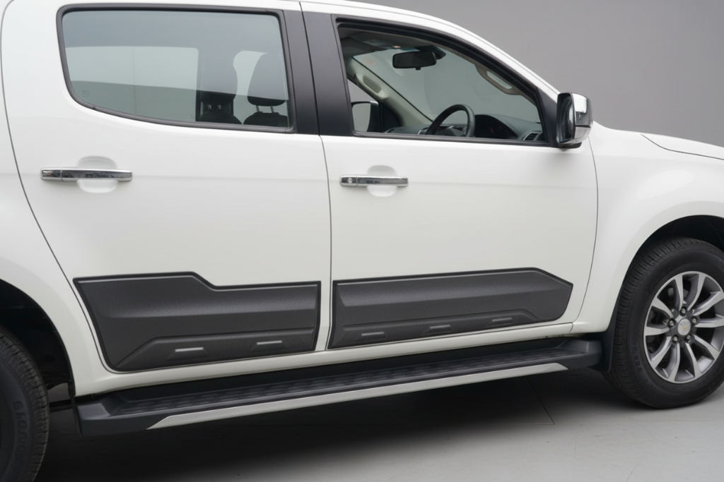 Close-up side view of a white pickup truck door with black trim, door handles, and black plastic lower body cladding.