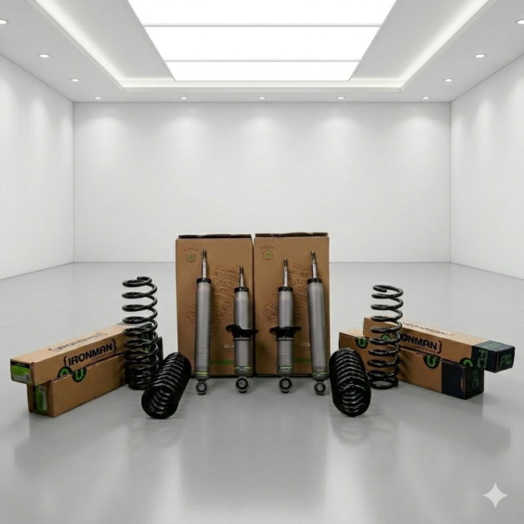 A set of automotive suspension components, including coil springs and shock absorbers, arranged in front of their cardboard packaging boxes on a clean white studio floor.