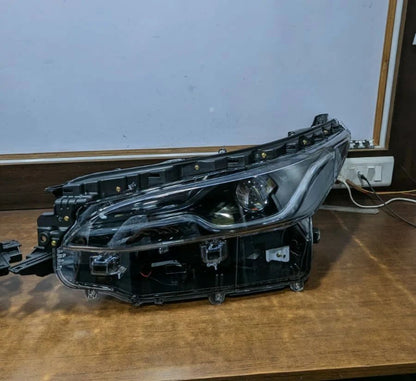 Car headlight assembly on a wooden surface with a white wall background