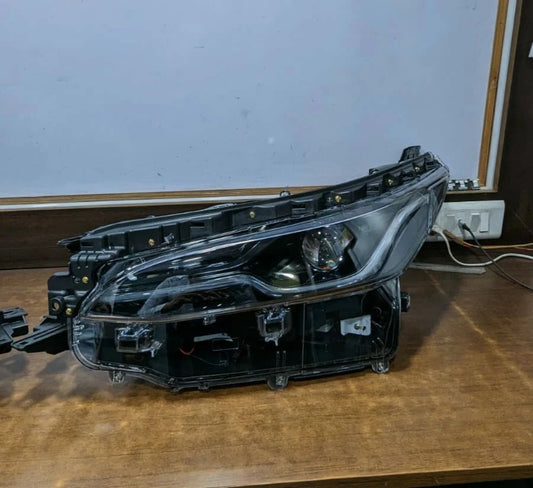 Car headlight assembly on a wooden surface with a white wall background